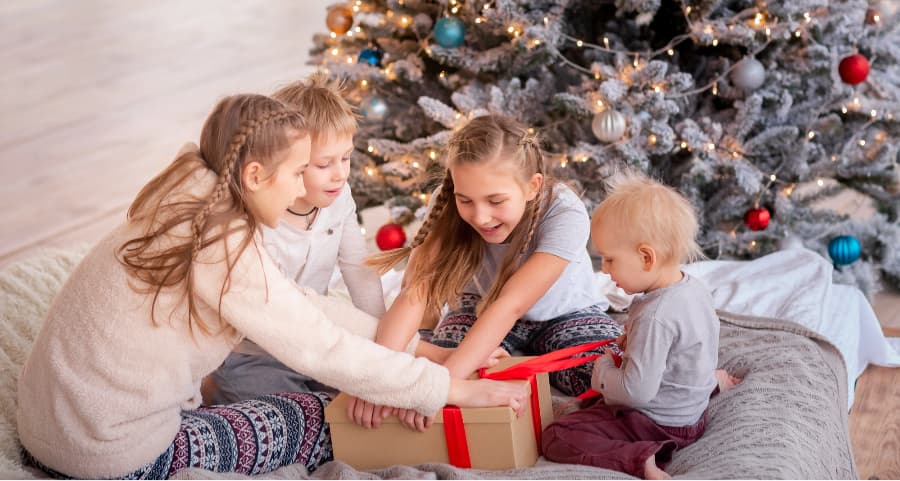 Siblings opening a present in the family room beside a Christmas tree.